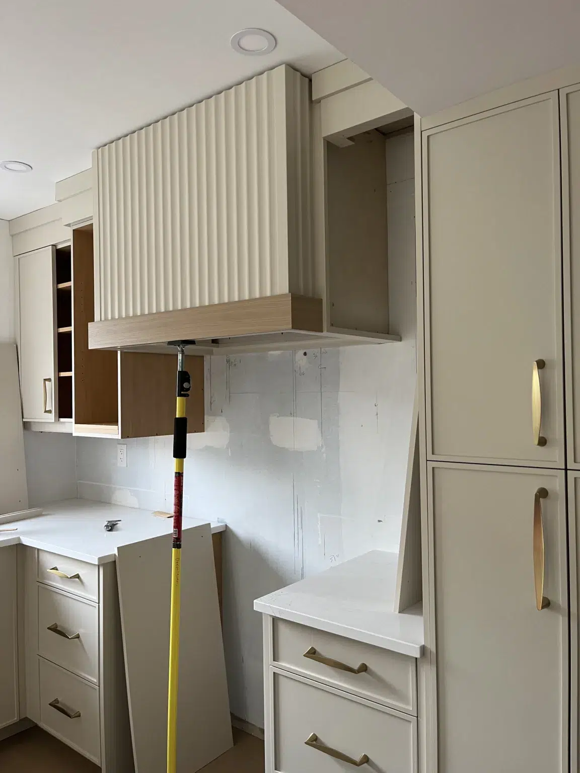 A contemporary kitchen in light brown tones, featuring wooden trim and gold handles, captured mid-renovation.