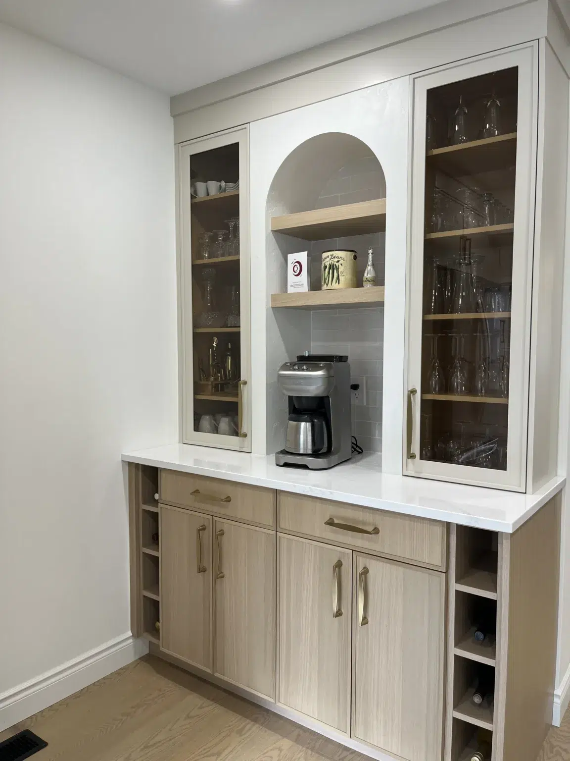 A close-up view of the drink station in a modern kitchen, showcasing light brown lower cabinets and white upper cabinets, both accented with gold handles.